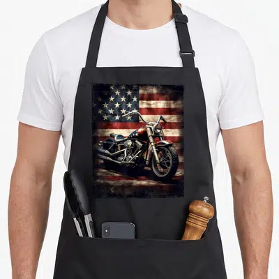 Tablier de cuisine noir avec illustration vintage d'une moto chopper devant une American Flag aux couleurs délavées et texturées.