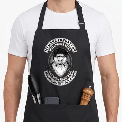 Tablier de cuisine noir avec illustration d'un vieil homme barbu au bandana et texte circulaire en noir et blanc.
