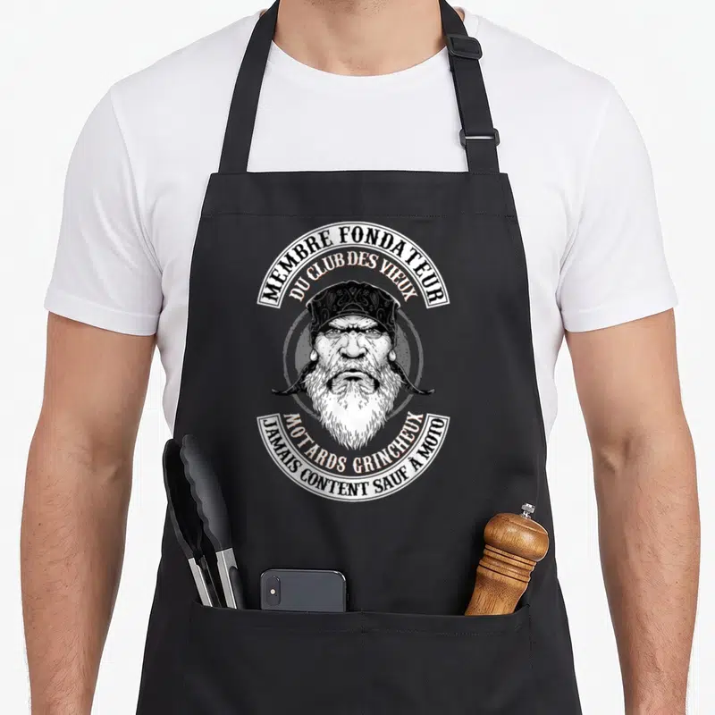 Tablier de cuisine noir avec illustration d'un vieil homme barbu au bandana et texte circulaire en noir et blanc.