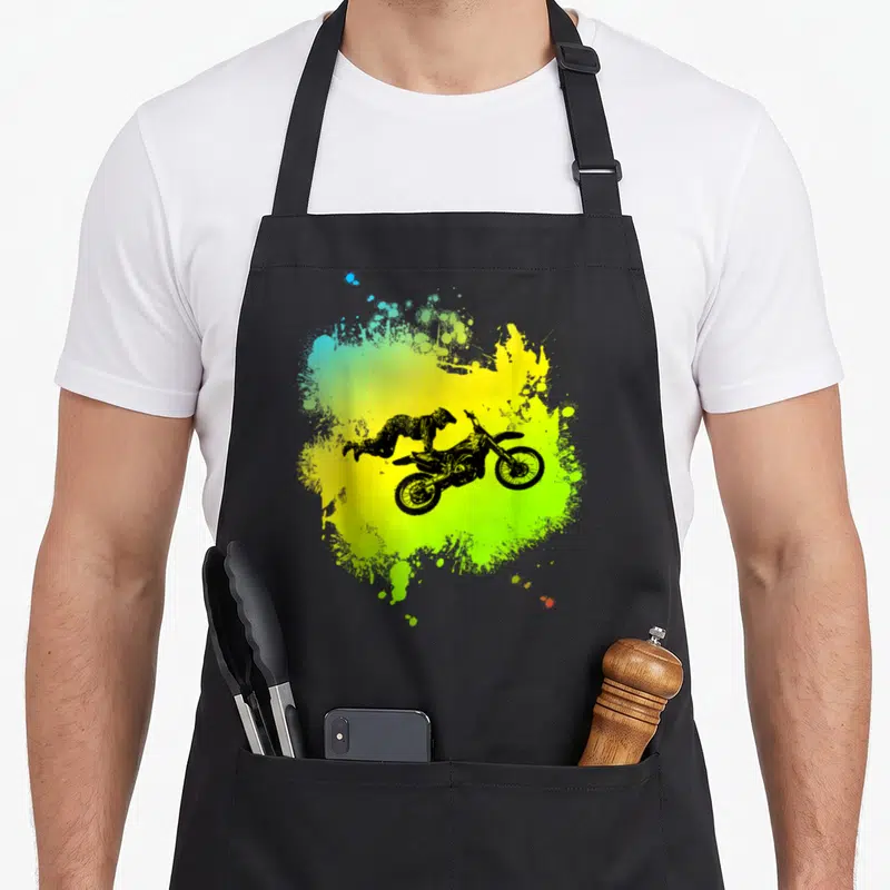 Tablier de cuisine noir avec illustration d'un pilote de motocross en l'air sur une tache de peinture jaune et verte.