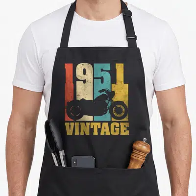 Tablier de cuisine noir avec motif vintage 1951 et silhouettes de motos colorées sur fond texturé.