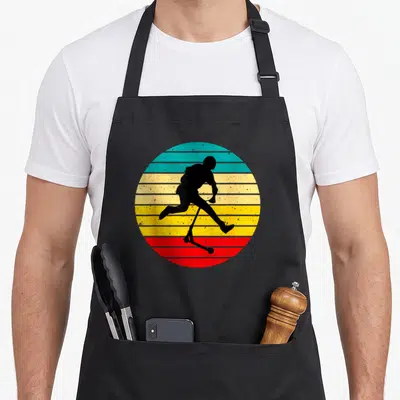 Tablier de cuisine noir avec silhouette noire de personne en acrobatie sur trotinette devant un cercle rayé coloré.