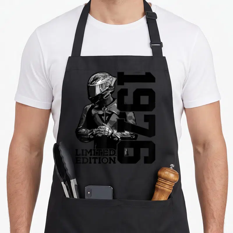 Tablier de cuisine noir avec illustration d'un pilote de moto casqué et les chiffres 1976 en grand format vertical.