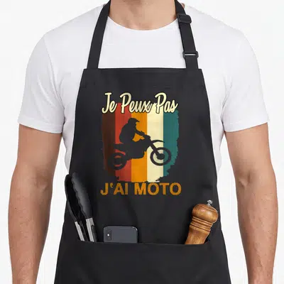 Tablier de cuisine noir avec une silhouette de motard et le texte Je Peux Pas J'ai Moto sur un fond rayé vintage.