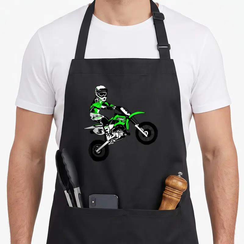 Tablier de cuisine noir avec une illustration colorée d'un pilote de Moto Cross pour enfants effectuant un saut aérien.