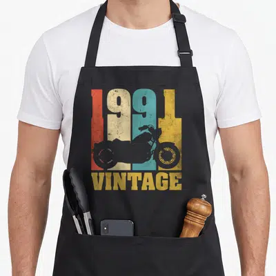 Tablier de cuisine noir avec design vintage 1991 et silhouette de moto multicolore.