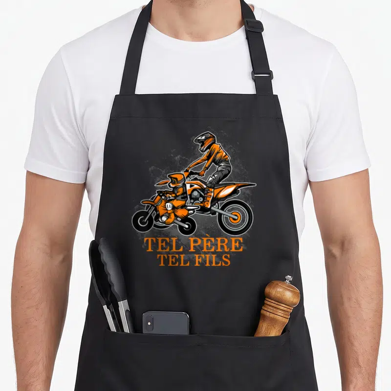 Tablier de cuisine noir avec illustration orange d'un père et fils motards sur dirt bike et le texte Tel Père Tel Fils en bas.