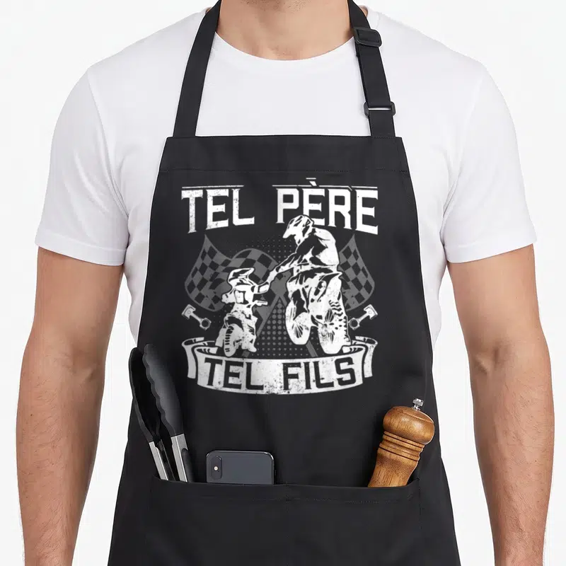 Tablier de cuisine noir avec illustration blanche Tel Père Tel Fils et silhouettes de motos cross sur fond de drapeaux à carreaux.
