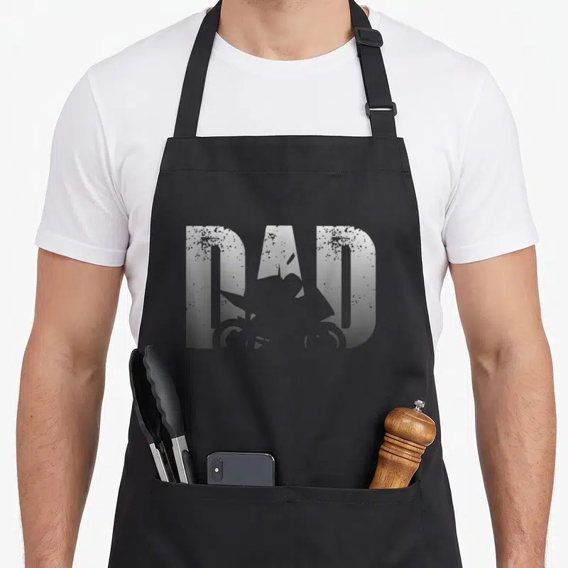 Tablier de cuisine noir avec l'inscription DAD en gris texturé intégrant la silhouette d'une moto biker dans les lettres.