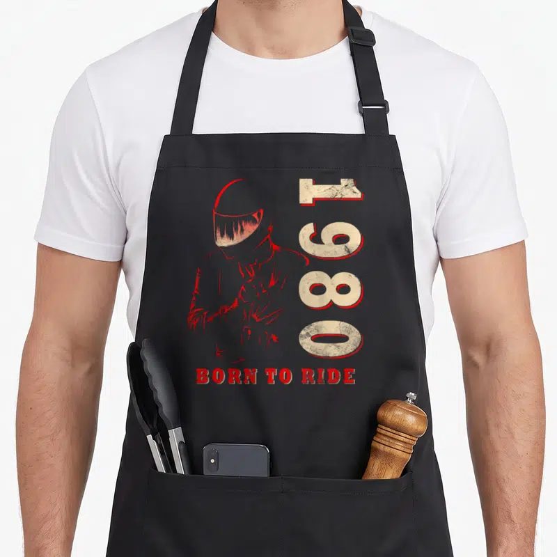 Tablier de cuisine noir avec illustration casque rouge, chiffres 1980 et texte Born to Ride en bas.