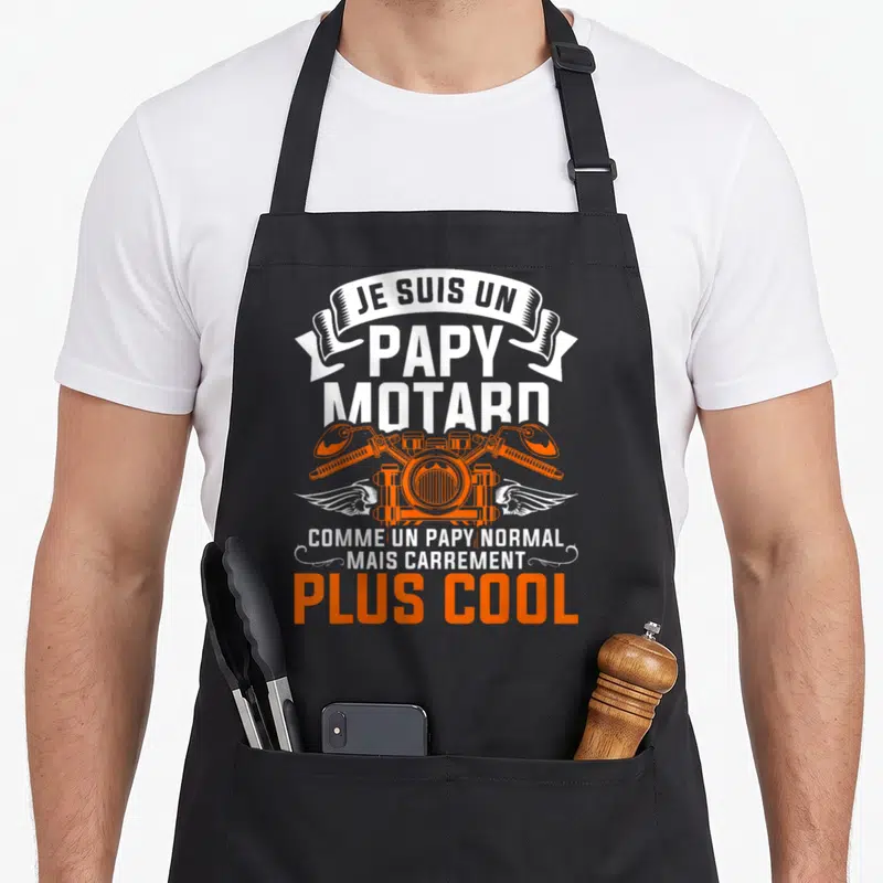 Tablier de cuisine noir avec inscription Je suis un papy motard et moteur orange stylisé aux ailes blanches.