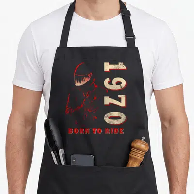 Tablier de cuisine noir avec illustration casque rouge, chiffres 1970 et texte Born to Ride imprimé en vintage.