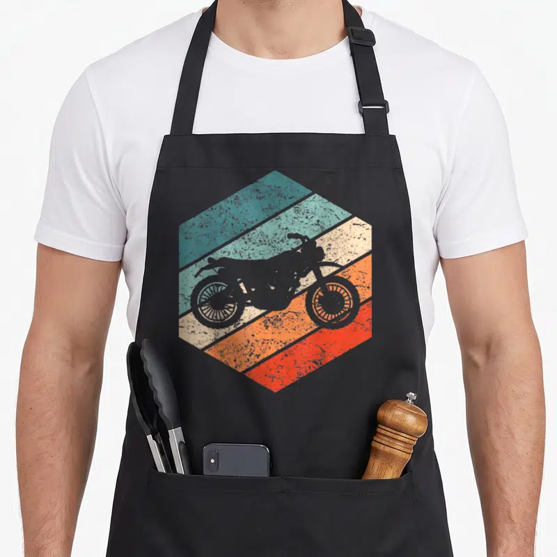 Tablier de cuisine noir avec motif hexagonal retro montrant une moto scrambler sur fond rayé multicolore.