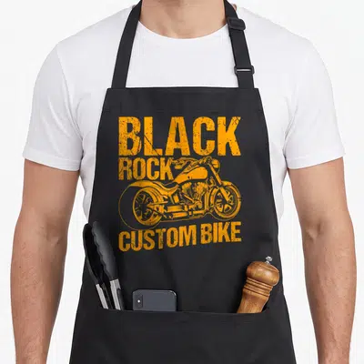 Tablier de cuisine noir avec illustration orange d'un chopper et le texte Black Rock Custom Bike en typographie usée.