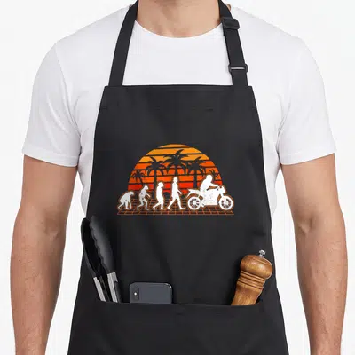 Tablier de cuisine noir avec illustration évolution humaine terminant par un motard sur fond de soleil orange et palmiers rétro.