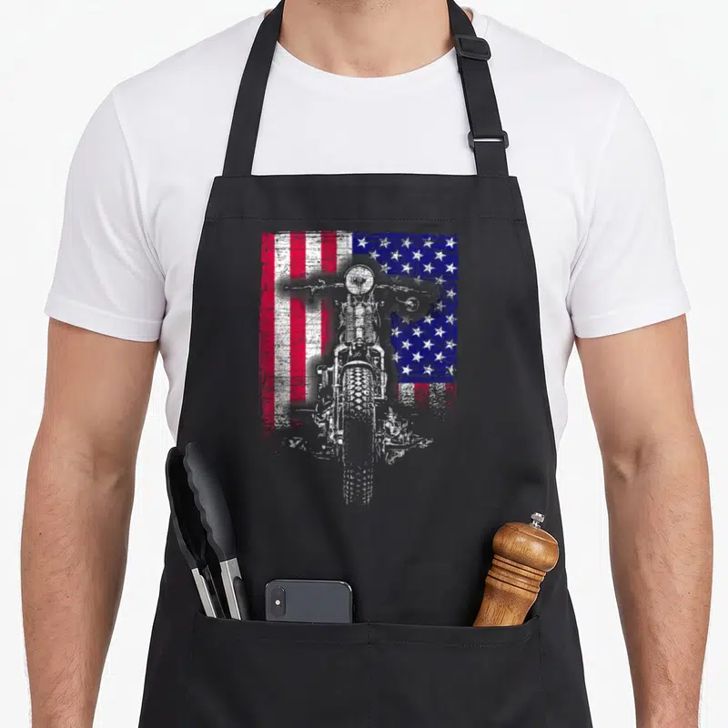 Tablier de cuisine noir avec illustration d'un motocycle devant un drapeau américain aux couleurs vives et effet vieilli.