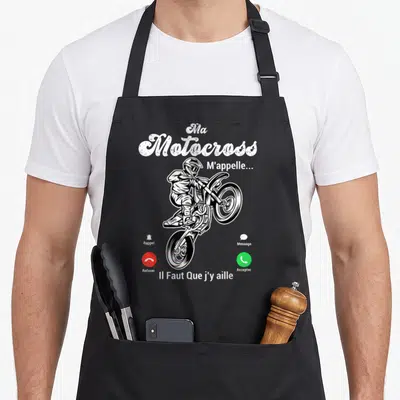 Tablier de cuisine noir avec illustration blanche d'un pilote de motocross effectuant un saut et du texte humoristique sur fond uni.