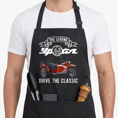 Tablier de cuisine noir avec illustration d'une moto Ural orange à side-car et texte blanc The Legend Drive the Classic.