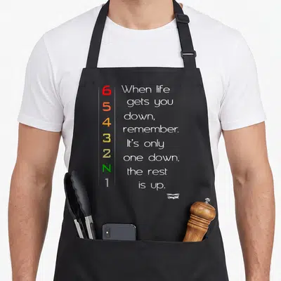 Tablier de cuisine noir avec boîte de vitesses colorée et texte When life gets you down imprimé en blanc.