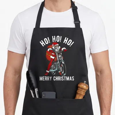 Tablier de cuisine noir avec illustration colorée du Père Noël en biker sur moto et texte blanc Ho. Ho. Ho. Merry Christmas.