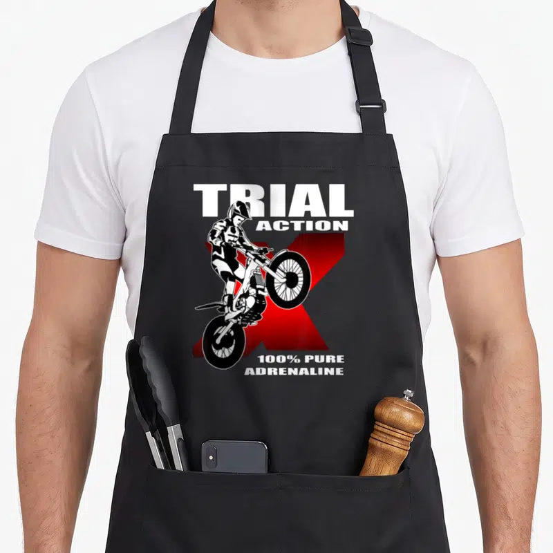 Tablier de cuisine noir avec illustration d'un pilote de trial sur fond de X rouge et texte blanc Trial Action 100% Pure Adrenaline