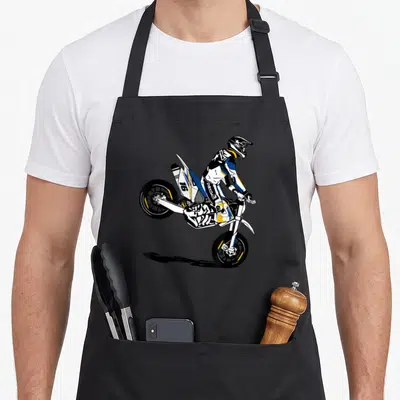 Tablier de cuisine noir avec illustration d'un supermotard en wheelie portant le dossard 16, style dessin animé dynamique.