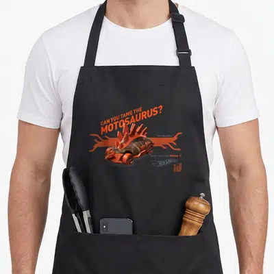 Tablier de cuisine noir avec une voiture dinosaure orange Hot Wheels et le texte Can You Tame The Motosaurus ?