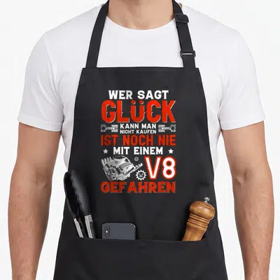 Tablier de cuisine noir avec texte Wer sagt Glück V8 Gefahren et illustration de moteur blanc sur fond uni.