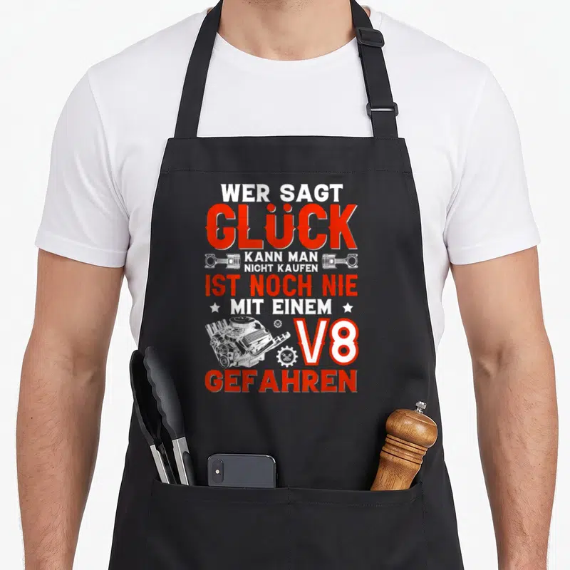 Tablier de cuisine noir avec texte Wer sagt Glück V8 Gefahren et illustration de moteur blanc sur fond uni.
