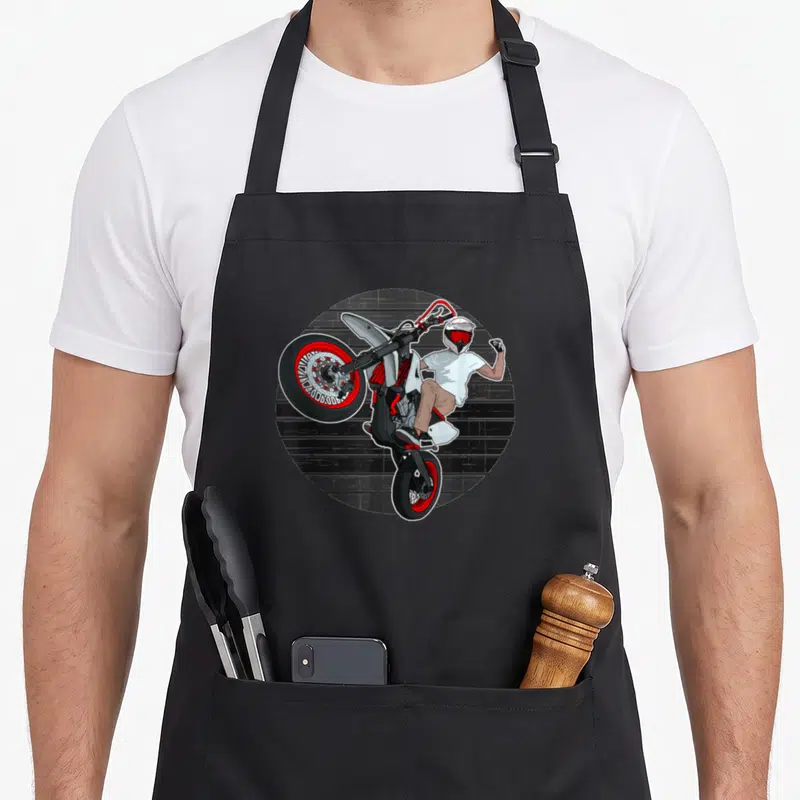 Tablier de cuisine noir avec illustration d'un supermoto en wheelie et d'un pilote en casque blanc.
