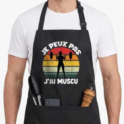 Tablier de cuisine noir avec silhouette soulevant une barre et texte Je peux pas j'ai muscu sur fond de soleil rétro.