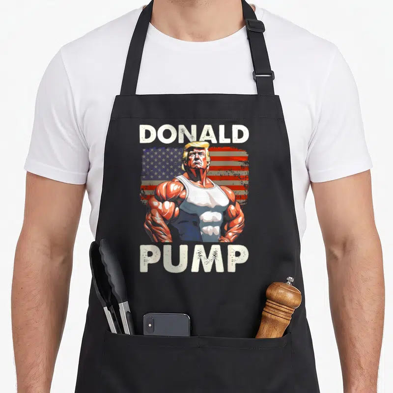Tablier de cuisine noir avec illustration musclée Donald Pump et drapeau américain en arrière-plan.