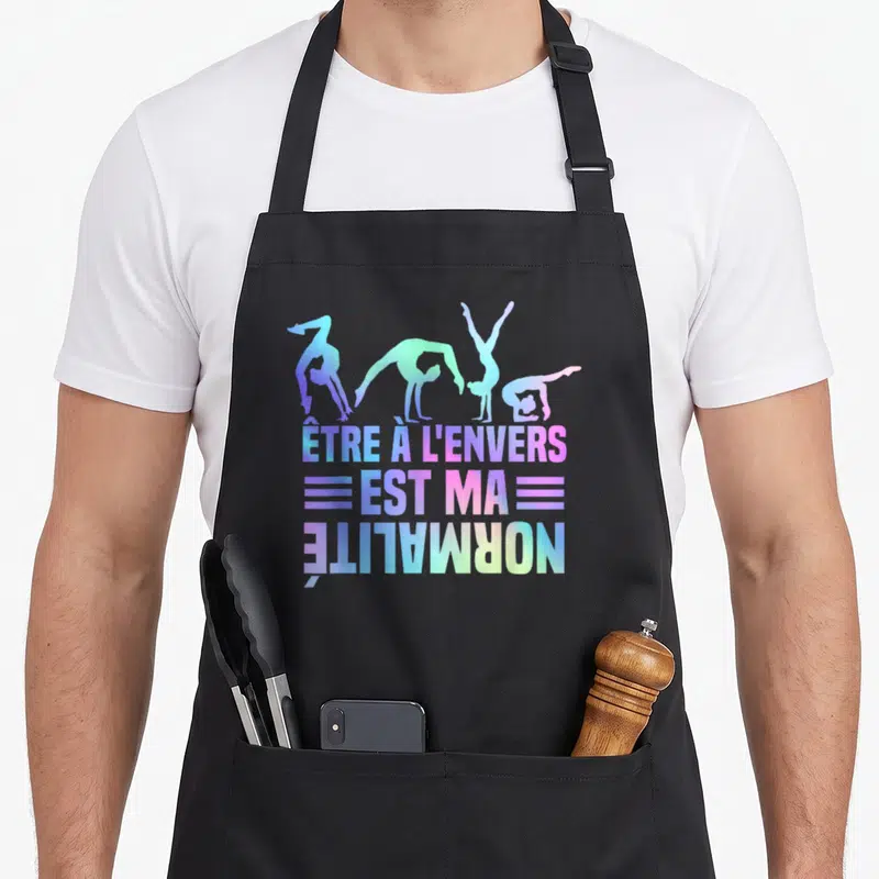 Tablier de cuisine noir avec quatre silhouettes de gymnastes et le texte être à l'envers est ma normalité en dégradé coloré.