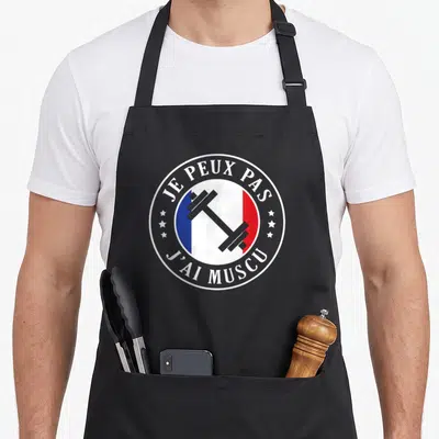 Tablier de cuisine noir avec logo circulaire Je Peux Pas J'ai Muscu et barre de poids sur fond tricolore.