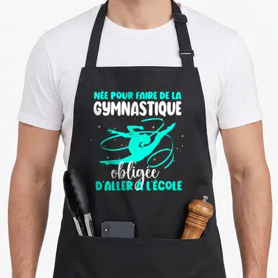 Tablier de cuisine noir avec une silhouette de gymnaste turquoise et le texte née pour faire de la gymnastique obligée d'aller à l'école.