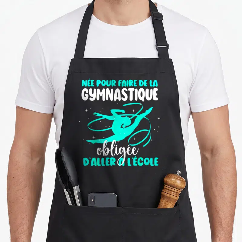 Tablier de cuisine noir avec une silhouette de gymnaste turquoise et le texte née pour faire de la gymnastique obligée d'aller à l'école.