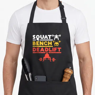 Tablier de cuisine noir avec les mots Squat Bench Deadlift et silhouettes d' haltérophiles en blanc jaune et rouge.