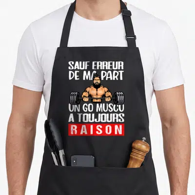 Tablier de cuisine noir avec un homme barbe soulevant une barre et le texte un go muscu a toujours raison en blanc et rouge.