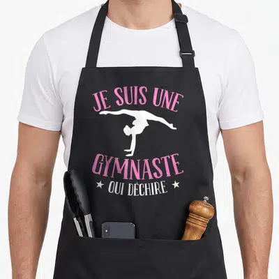 Tablier de cuisine noir avec silhouette blanche de gymnaste et texte rose Je Suis Une Gymnaste Qui Déchire.