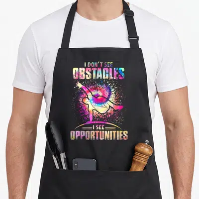Tablier de cuisine noir avec illustration colorée d'un athlète en mouvement et texte I don't see obstacles I see opportunities.