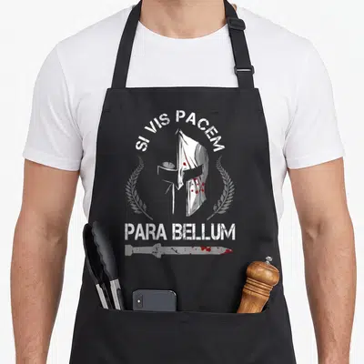 Tablier de cuisine noir avec illustration d'un casque de guerrier, d'une épée et le texte Si Vis Pacem Para Bellum en blanc et rouge.