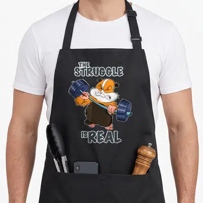 Tablier de cuisine noir avec un cochon d'Inde orange et blanc soulevant une barre de poids bleue.