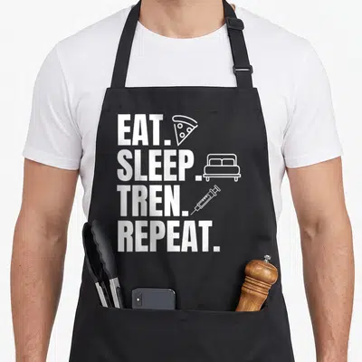 Tablier de cuisine noir avec texte blanc Mangez Dormez Tren Repeat et icônes pizza lit seringue.