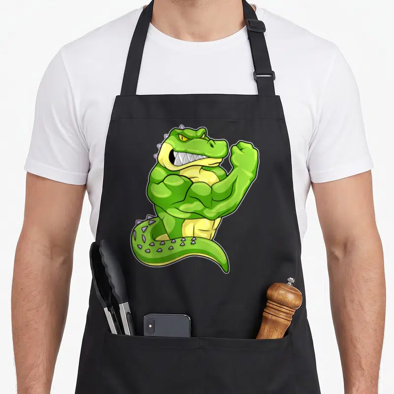 Tablier de cuisine noir avec un crocodile bodybuilder vert aux muscles saillants et une expression féroce.