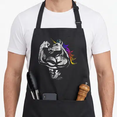 Tablier de cuisine noir avec illustration d'une licorne musclée aux cheveux multicolores et effet vieilli blanc.