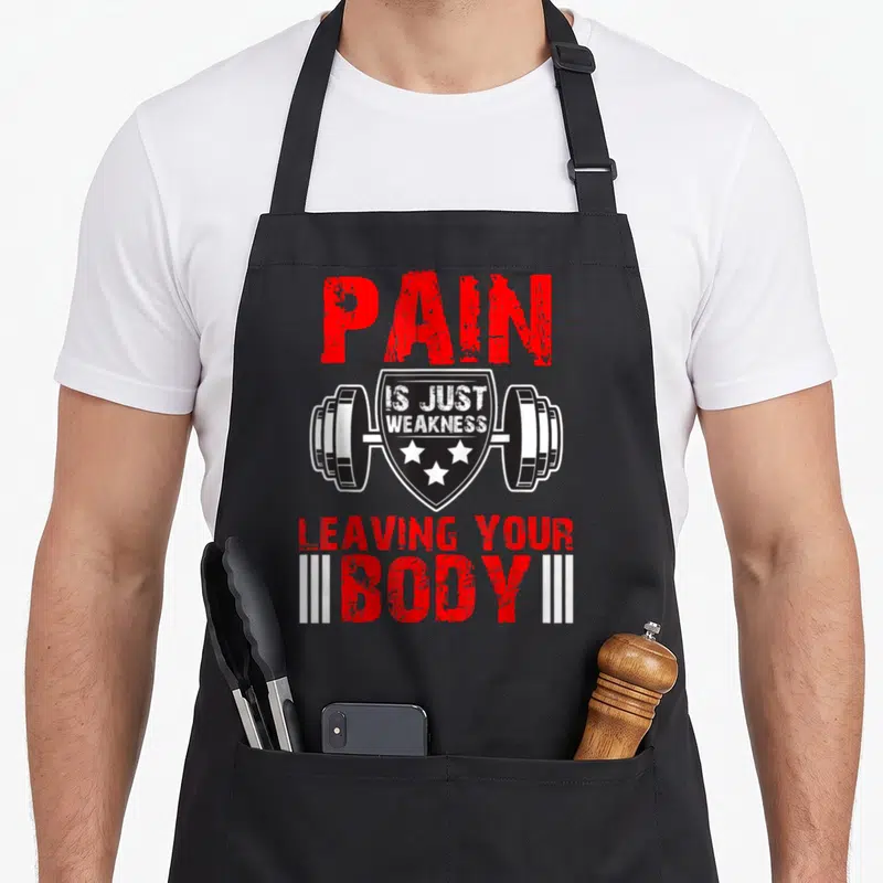 Tablier de cuisine noir avec inscription PAIN IS JUST WEAKNESS LEAVING YOUR BODY et barre d'haltère.