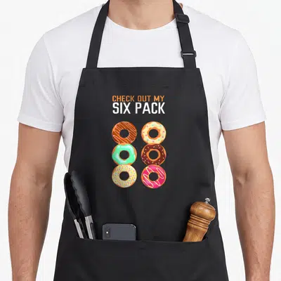 Tablier de cuisine noir avec six beignets colorés et le texte Check out my Six Pack imprimé en haut.