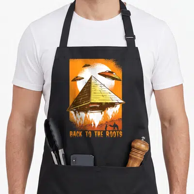 Tablier de cuisine noir avec une pyramide flottante, des ufo et le texte back to the roots en orange.