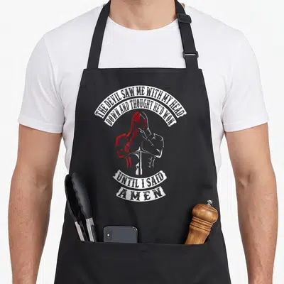 Tablier de cuisine noir avec illustration d'un chevalier en prière et texte blanc sur fond gris uni.
