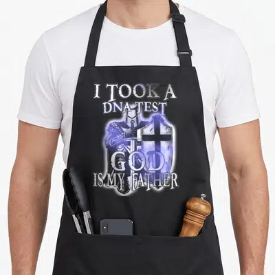 Tablier de cuisine noir avec illustration d'un chevalier Templier tenant épée et bouclier, entouré du texte « I took a DNA test God is my father » en lettres stylisées violettes et blanches.